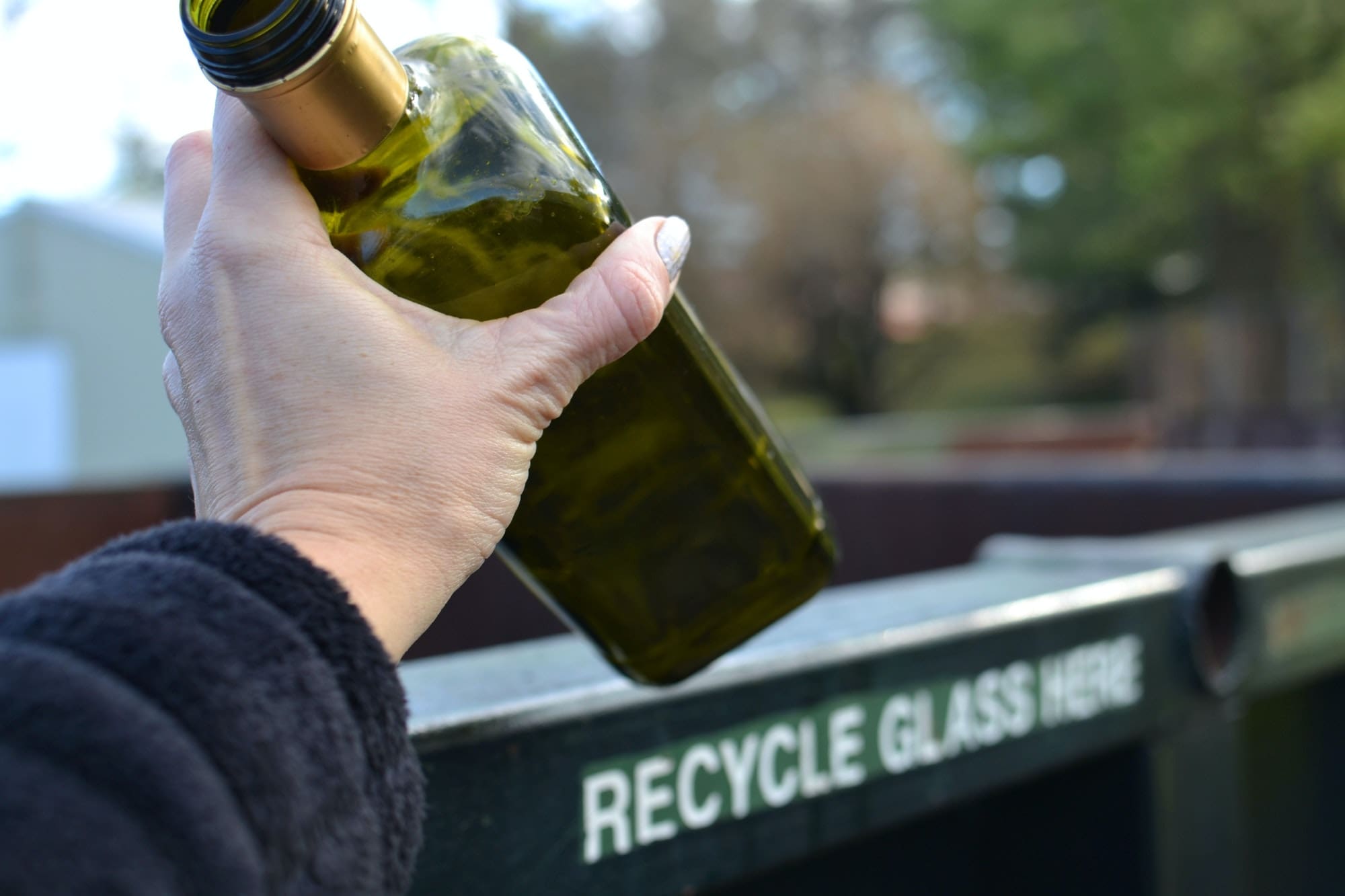 Eco-Friendly Waste Disposal: Hand placing a glass bottle into a recycling dumpster.